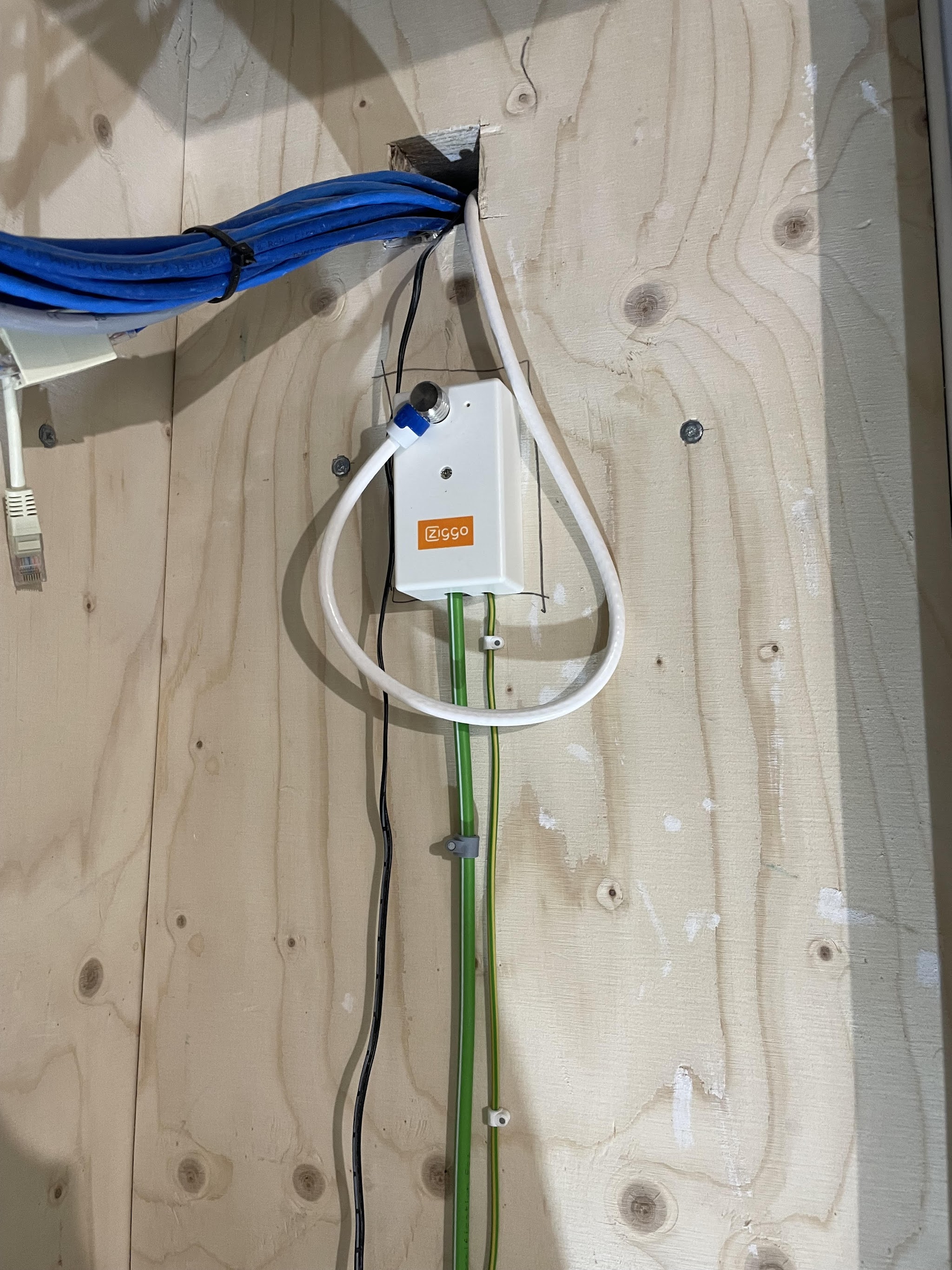 Bundel blauwe UTP-kabels en een glasvezelaansluiting op een houten wand