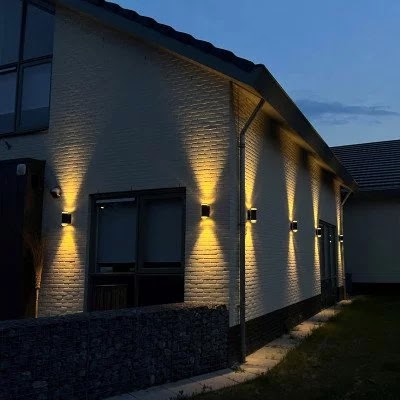 Gevel van een huis in de schemering met wandlampen die licht omhoog en omlaag geven